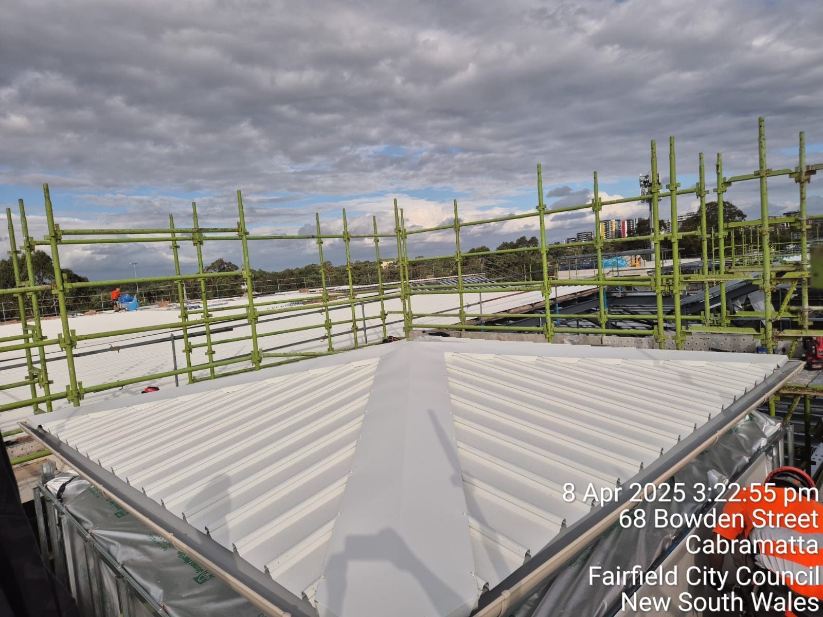 Construction site with corrugated roof panels and bamboo scaffolding under a cloudy sky