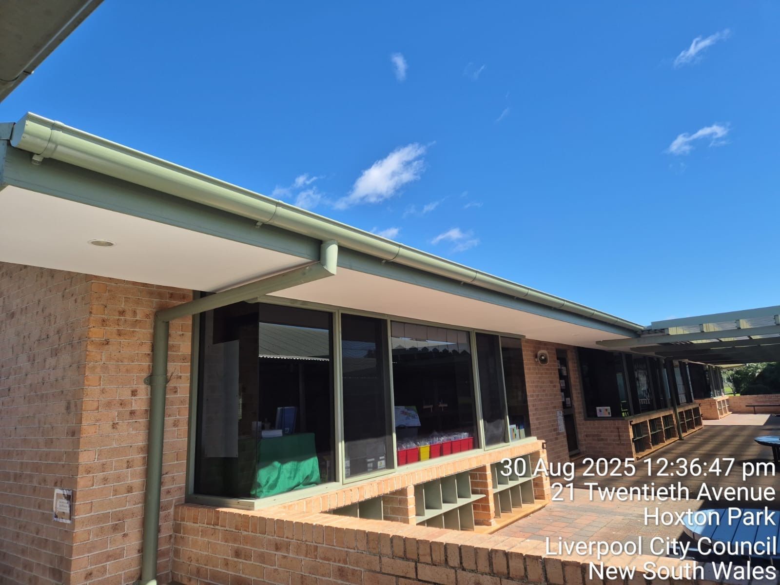 Brick school walkway with large windows, green roof trim, and blue sky overhead