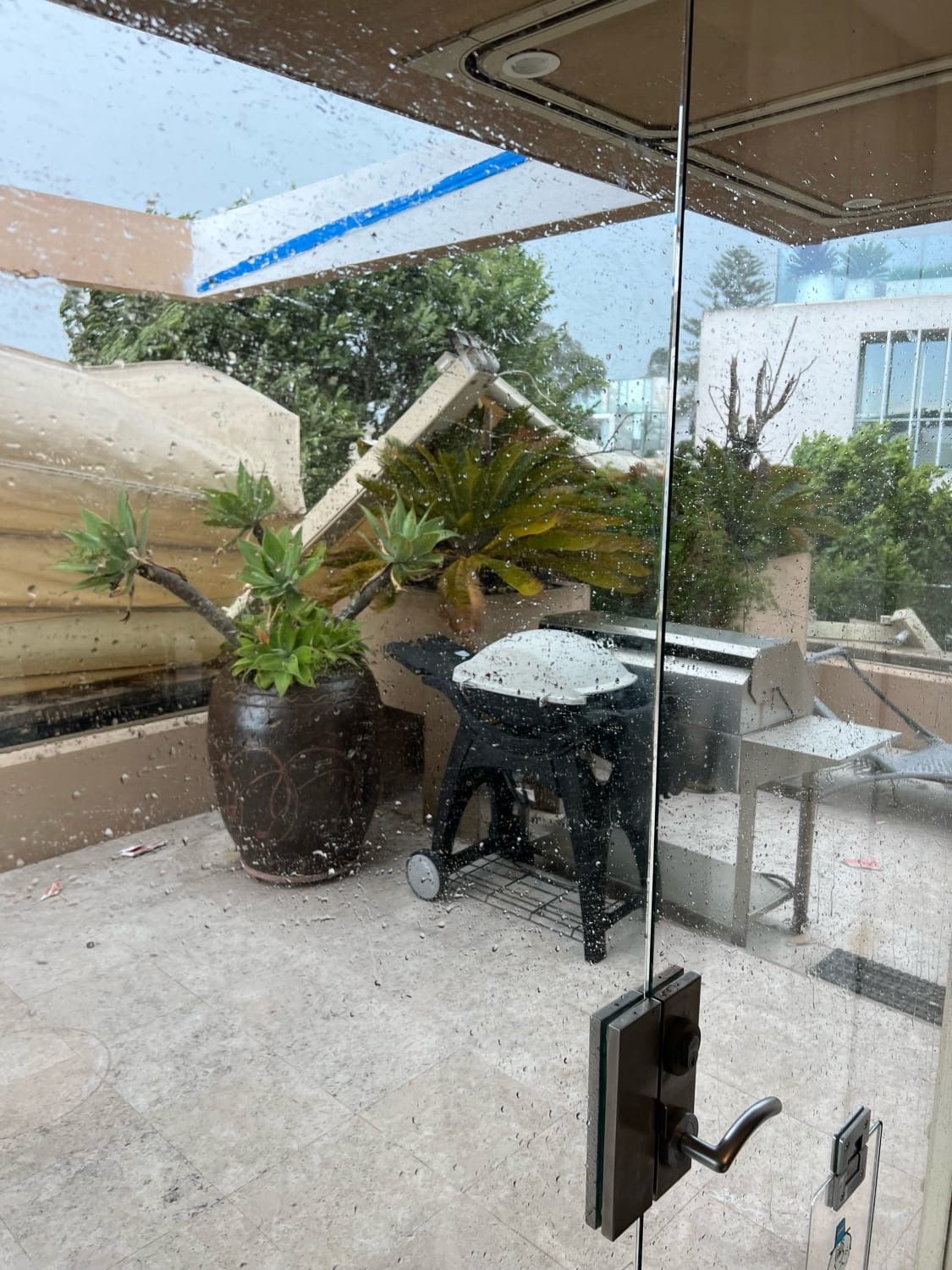 Patio with glass door, potted plants, outdoor grill, and chairs overlooking a garden