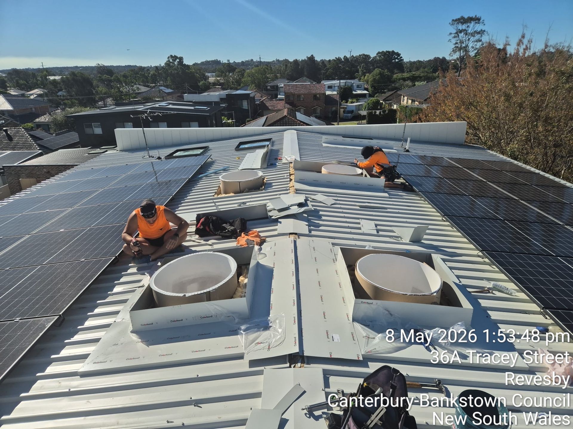 Worker in orange safety gear fastening a roof sheet on a suburban house roof