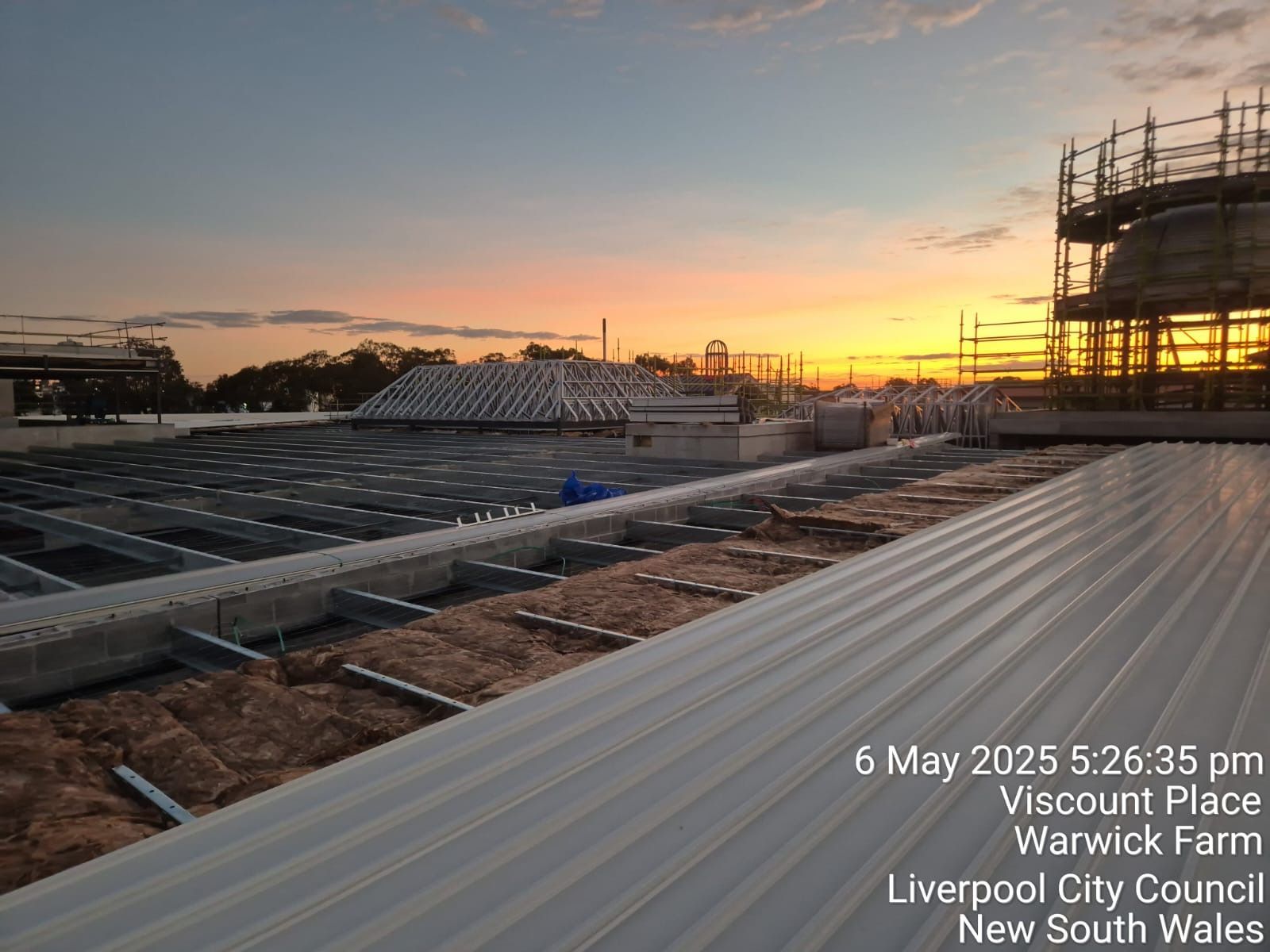 Rooftop construction site at sunset with corrugated metal roofing and scaffolding silhouettes