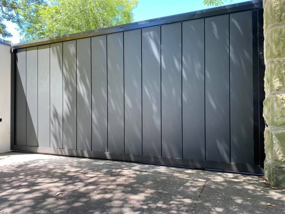 Modern gray garage doors with vertical panels beside a stone wall in a sunny driveway