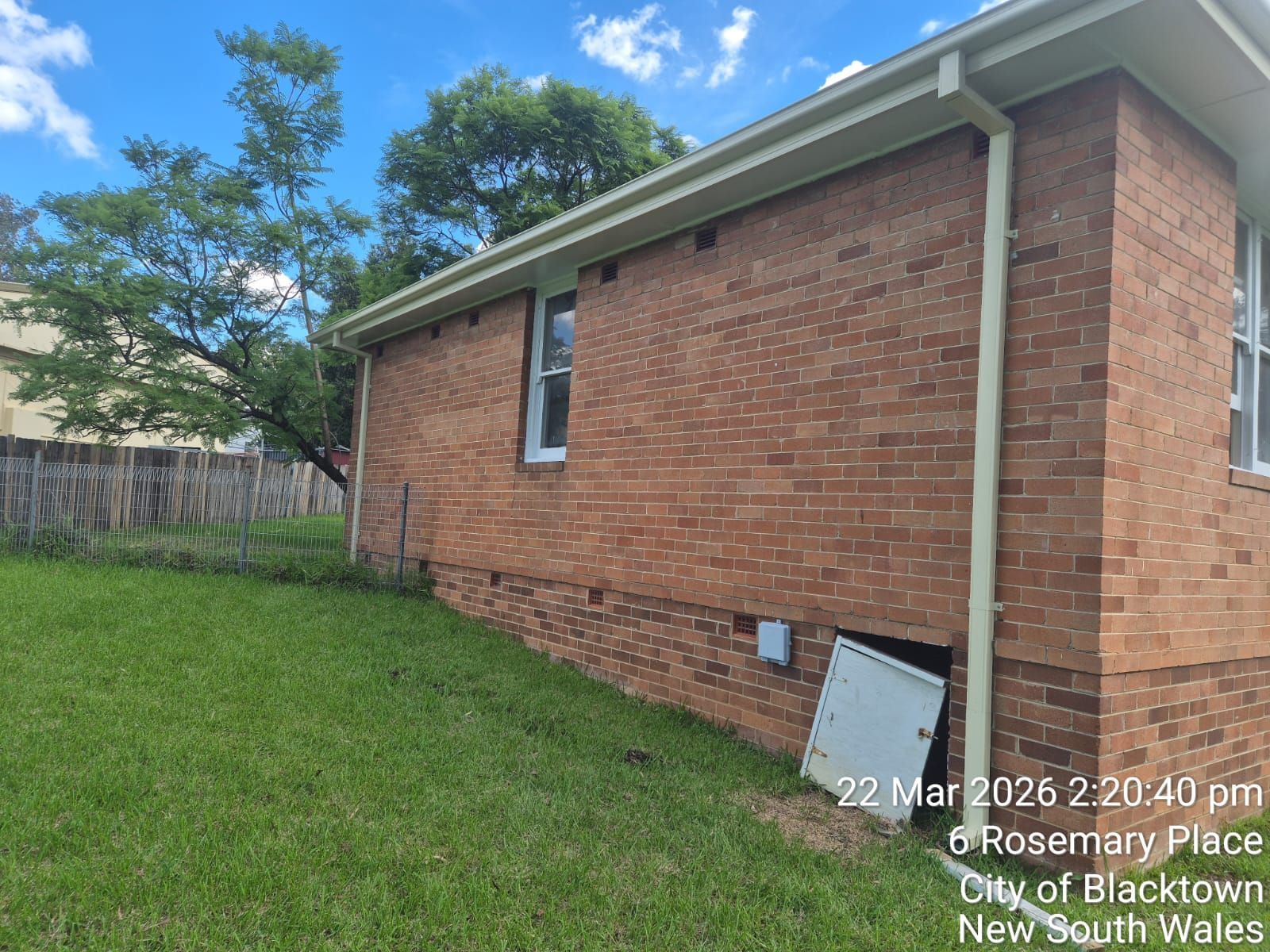Brick house exterior with green lawn, side window, and partly visible basement vent under blue sky