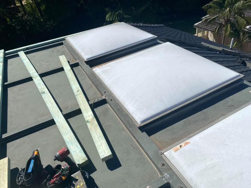 Rooftop with three large white skylights and stacked lumber beside a worker near the edge