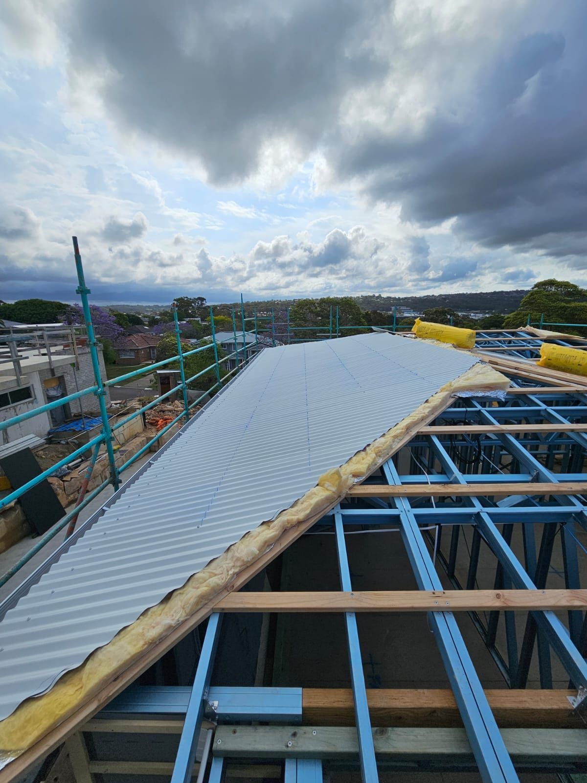 Roof construction with corrugated metal sheets on a blue steel frame under a cloudy sky