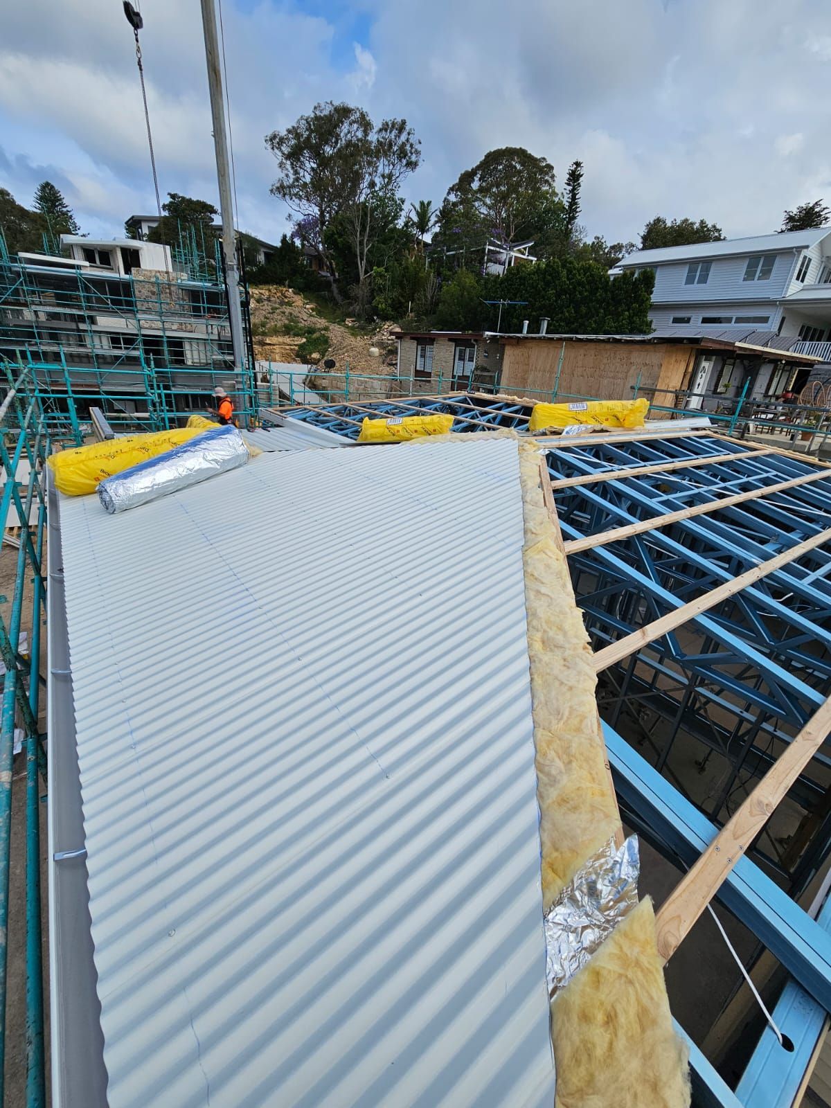 Corrugated metal roof under construction with scaffolding, plywood beams, and yellow safety covers