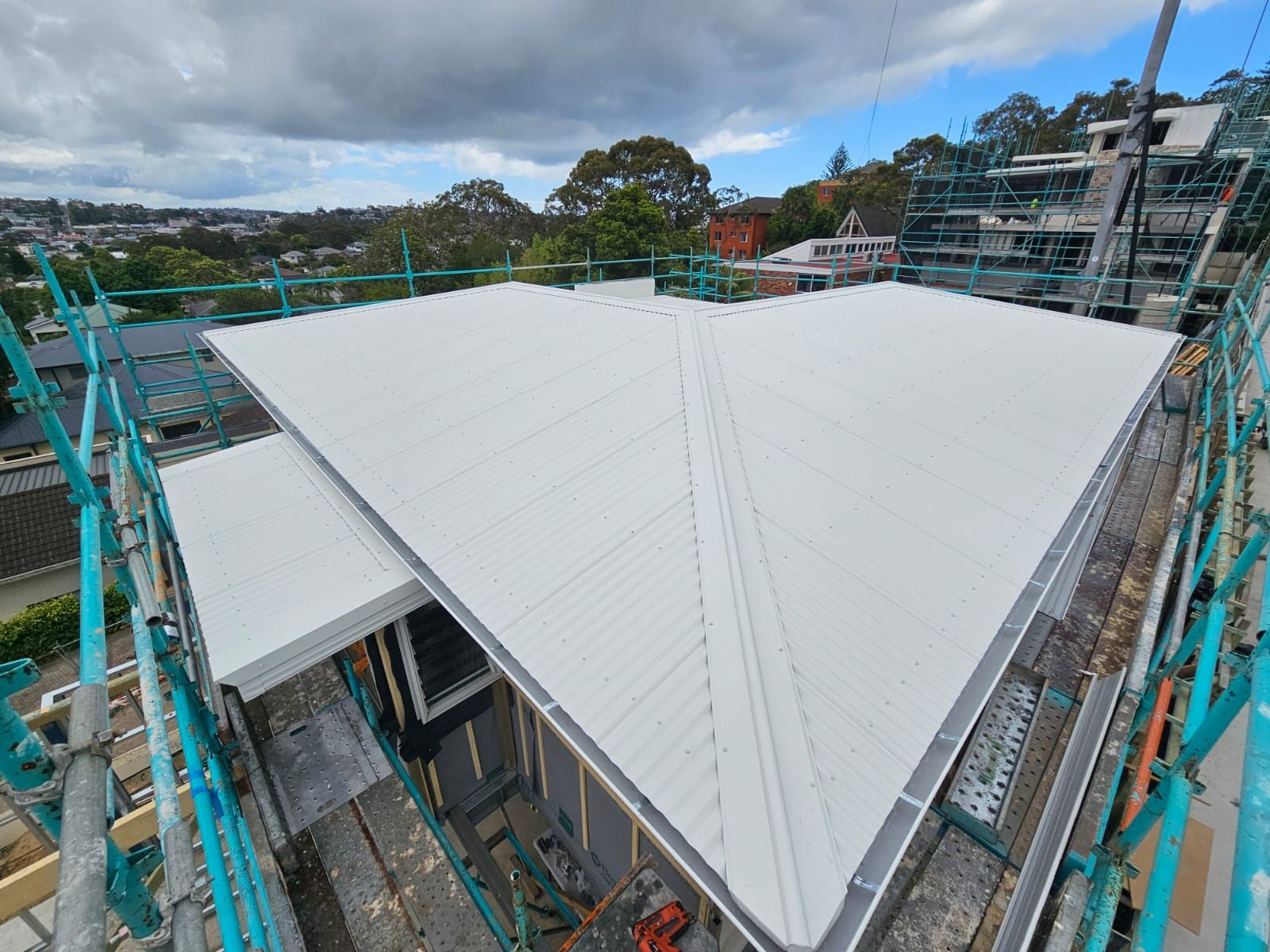 White metal roof under construction, seen from above with turquoise scaffolding around the building.