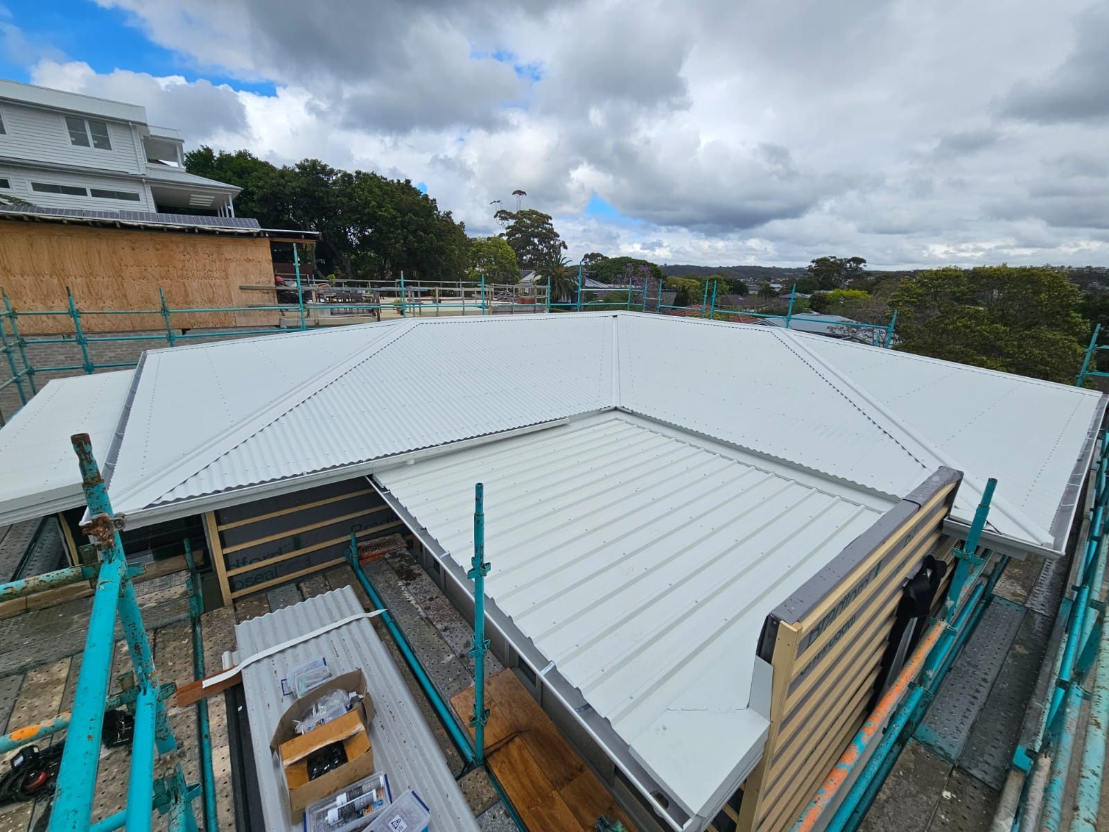 Rooftop with a new light-gray metal roof under construction, with scaffolding and cloudy sky.