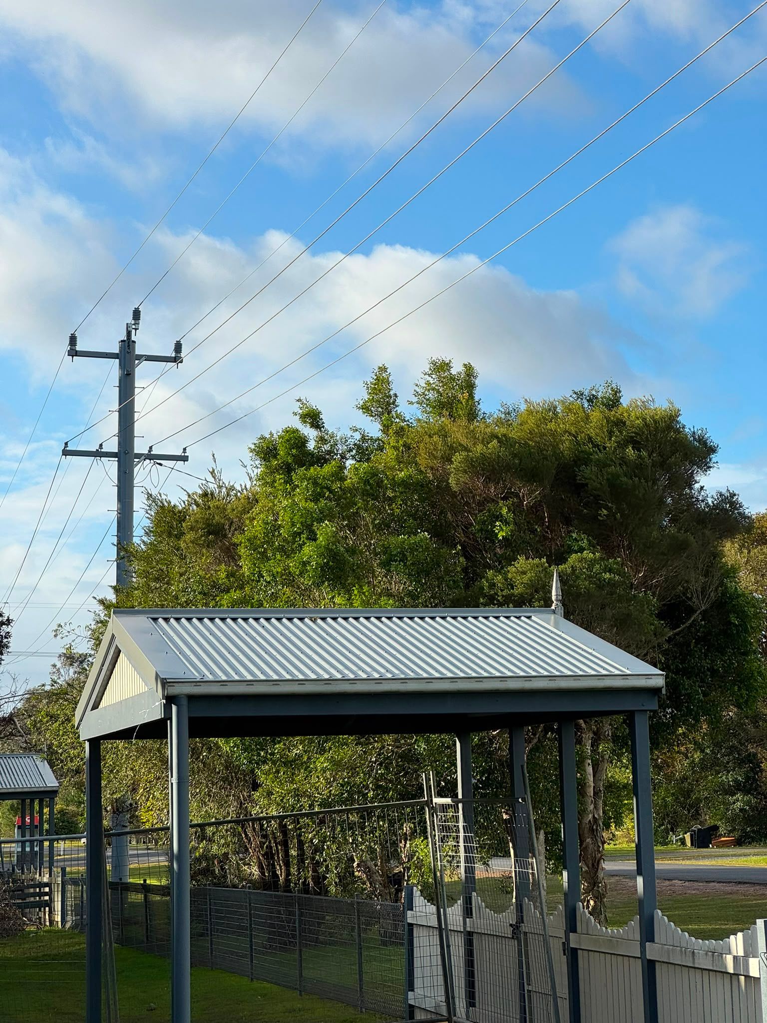 Small shed with corrugated metal roof beside a utility pole under a blue sky
