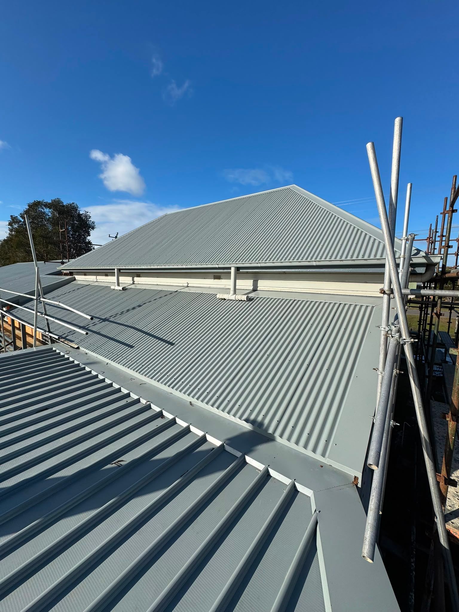 Corrugated metal roof under construction with scaffolding against a blue sky