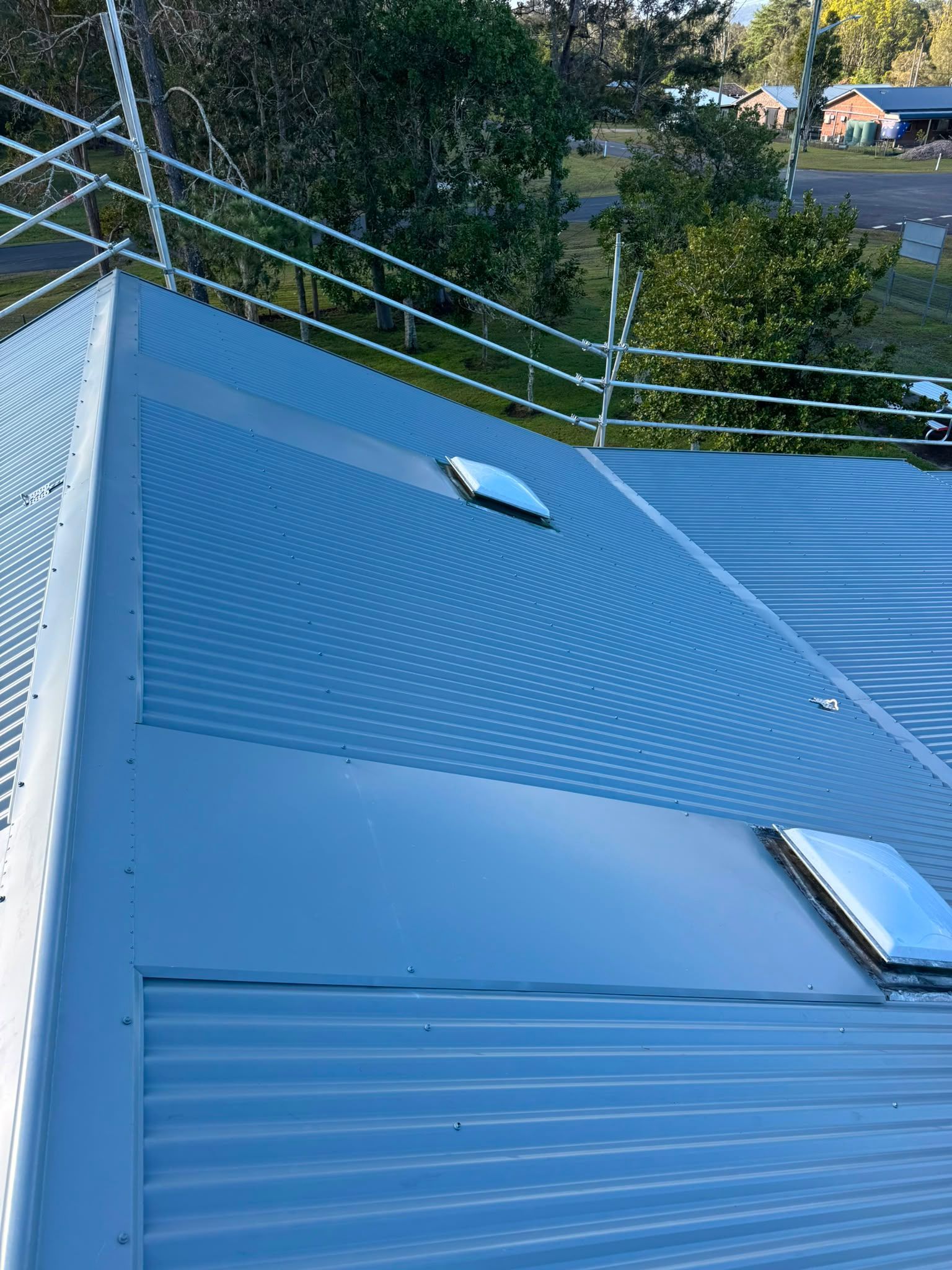 Blue metal rooftop with vents and railings beside trees at dusk