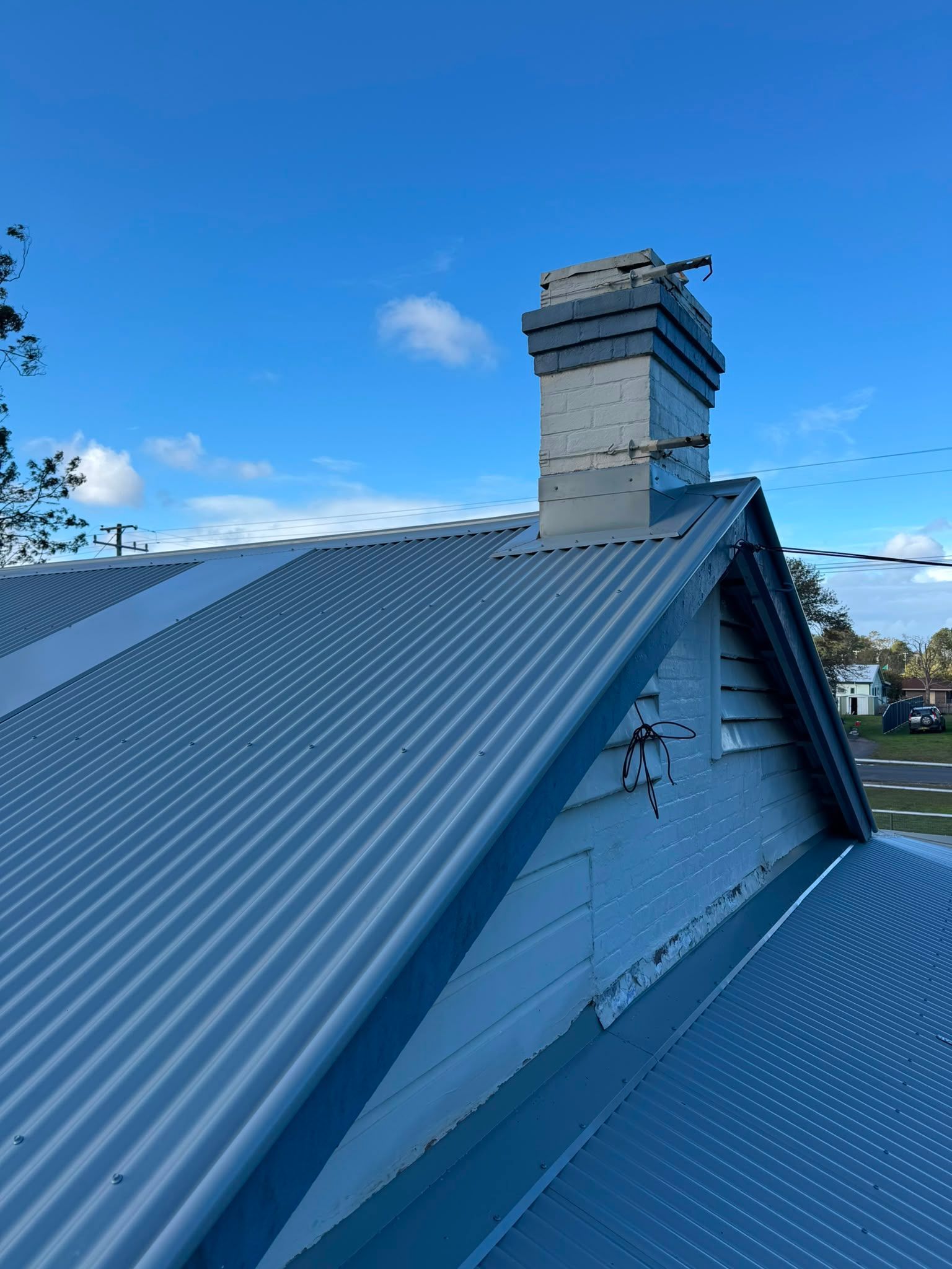 Blue metal roof with a brick chimney under a clear sky