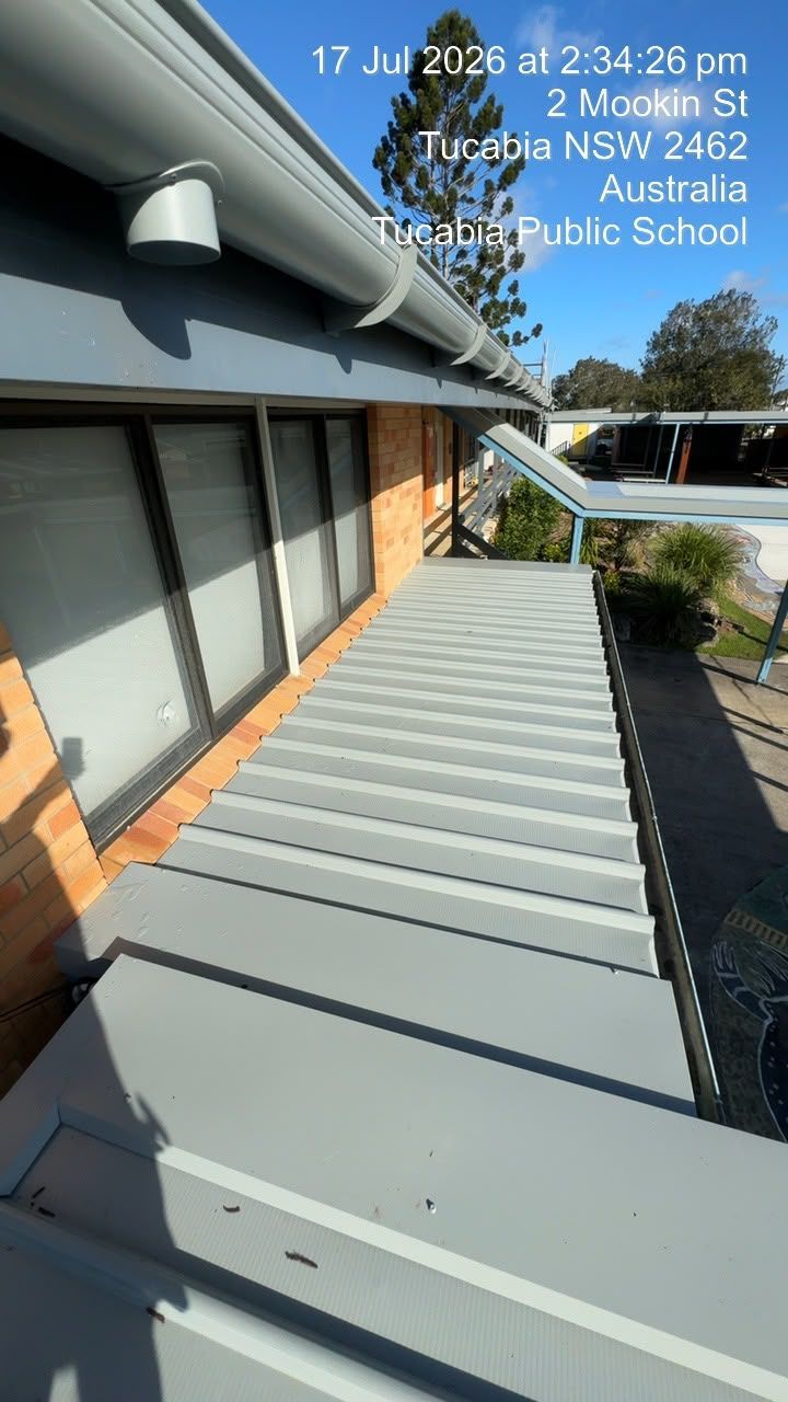 Steep gray metal roof beside a school building, with windows and solar roof vents under a blue sky.