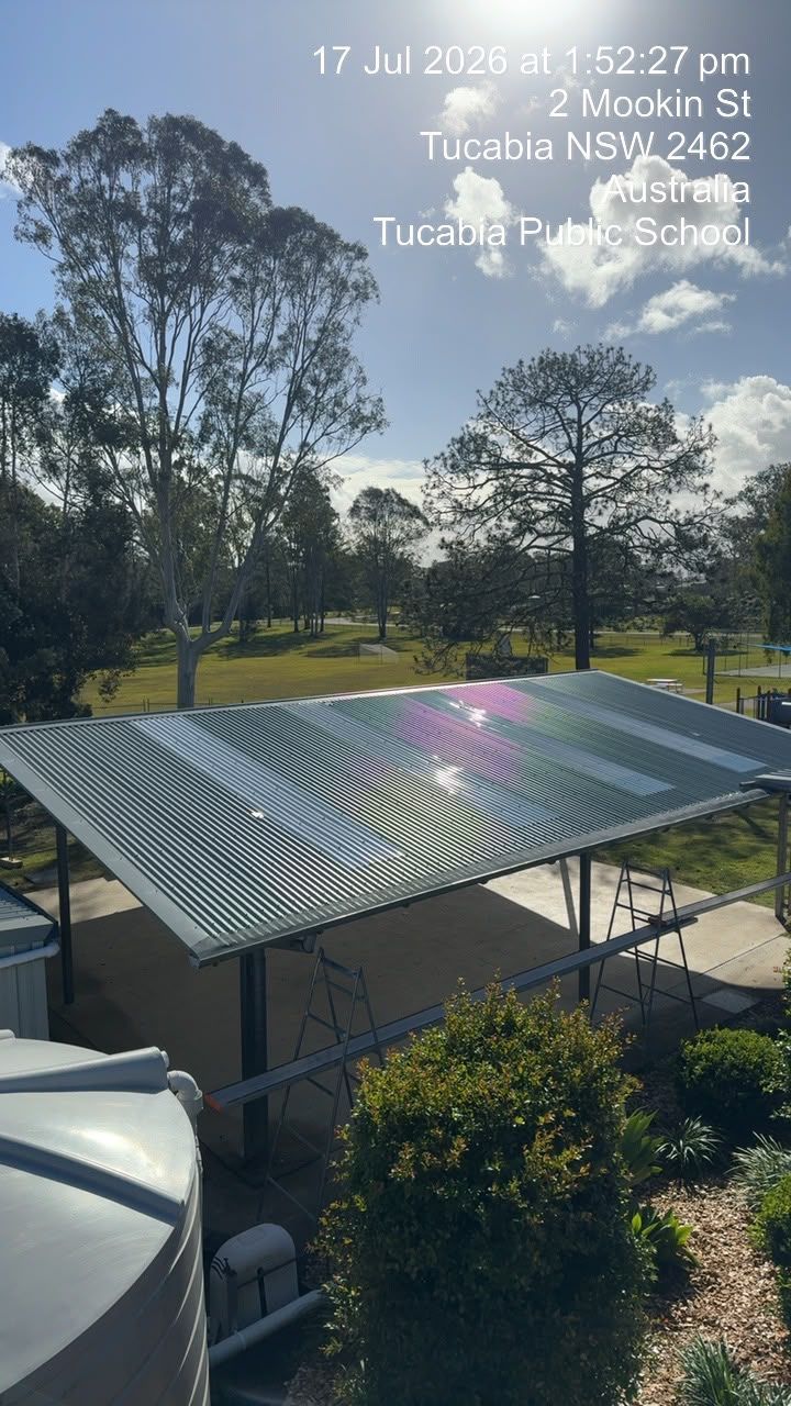 Solar panels on a metal frame in a sunny yard with trees and blue sky.