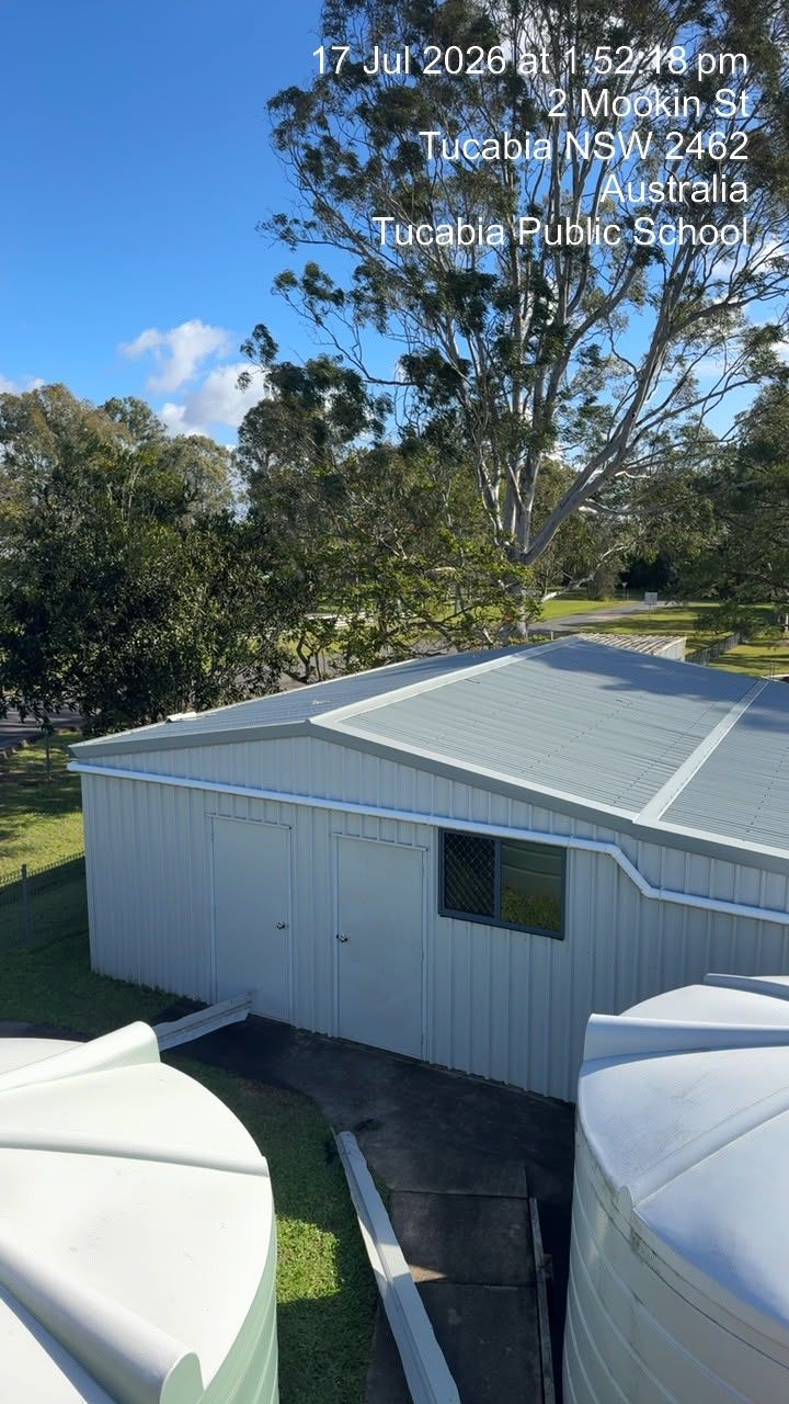 White-roofed shed beside two white tanks, surrounded by trees under a blue sky