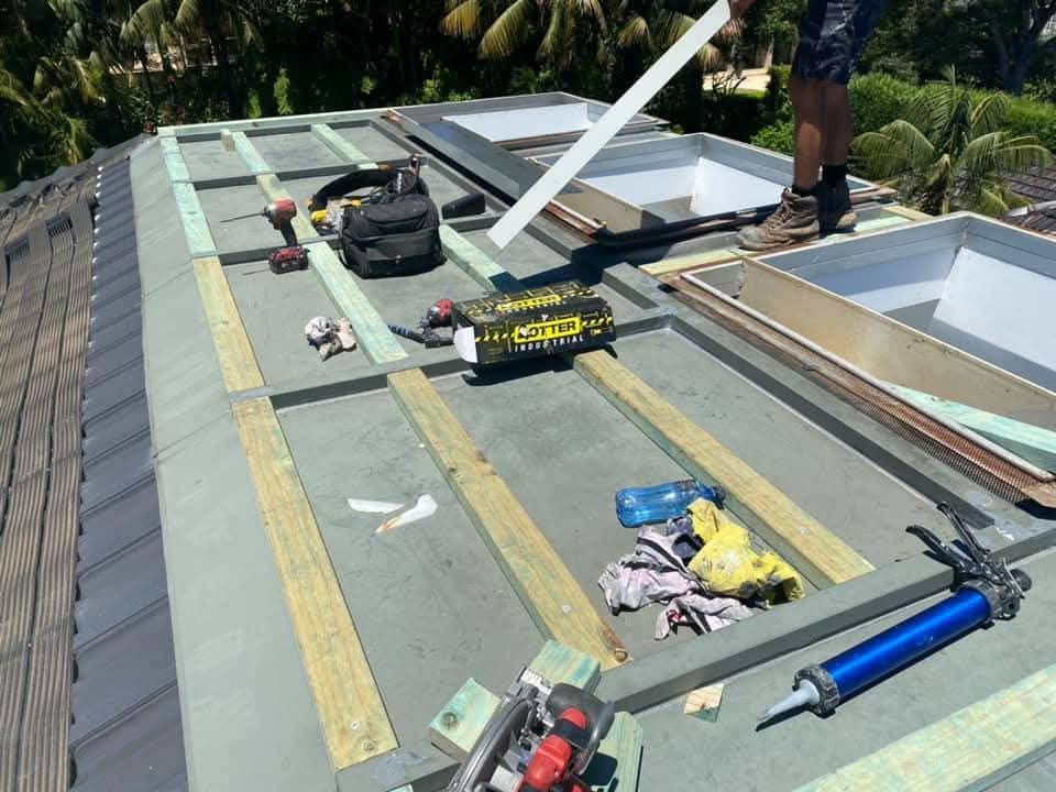 Roof under repair with tools, shingles, and two workers near a skylight opening