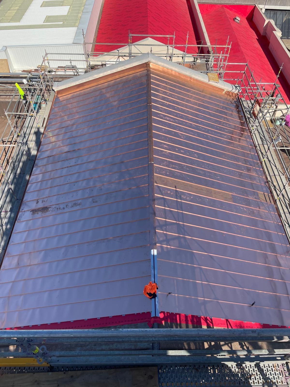 Roof under construction with dark panels, surrounded by scaffolding and red protective sheeting