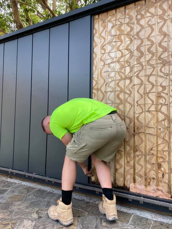 Person in a neon green shirt bends over beside a black wall and tan patterned panel outdoors.