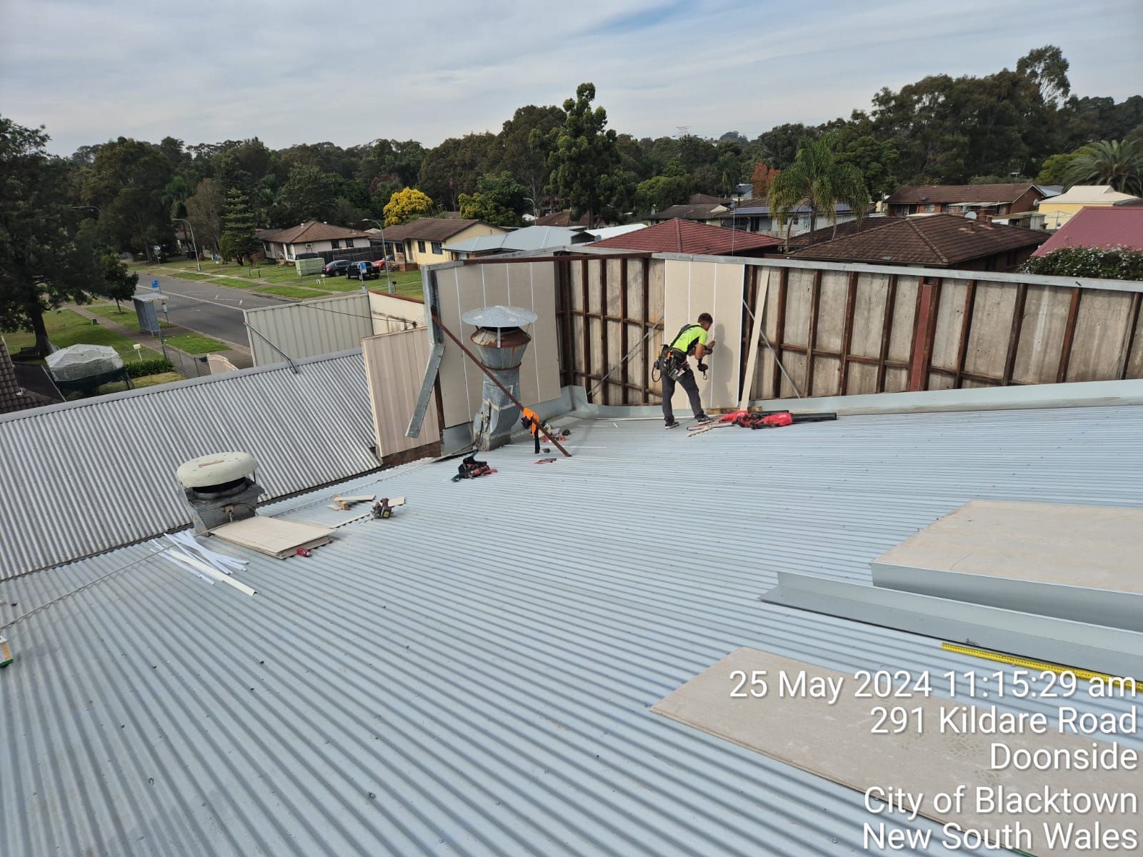 Workers on a corrugated metal roof repairing a building in a suburban neighborhood.