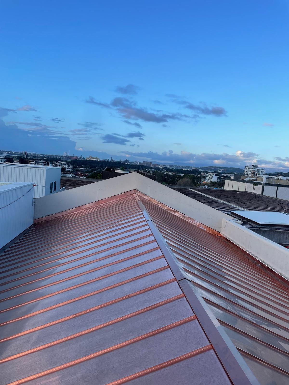 View from a metal rooftop at sunset, overlooking a city skyline and blue sky