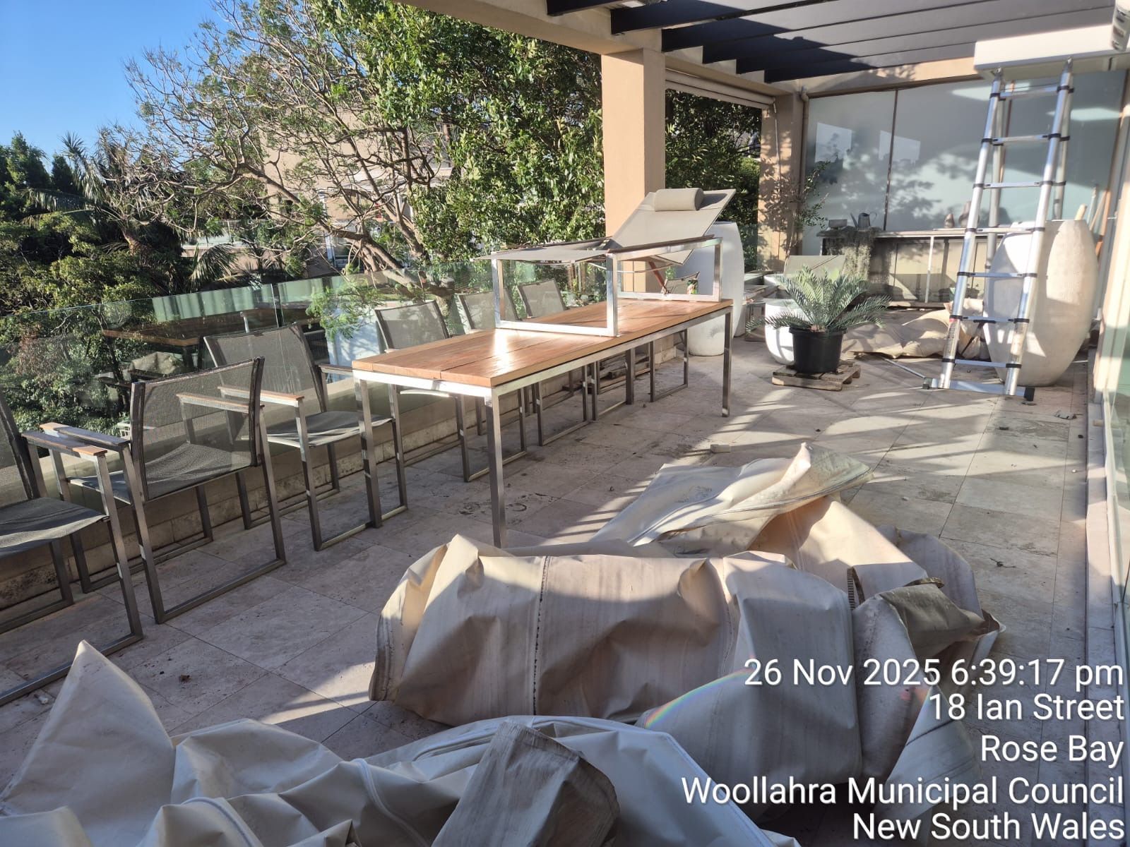 Sunlit patio with outdoor dining table, chairs, grill, and covered furniture under a pergola