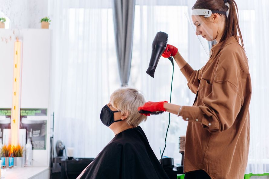 Stylist blow-dries a seated client’s hair in a bright salon
