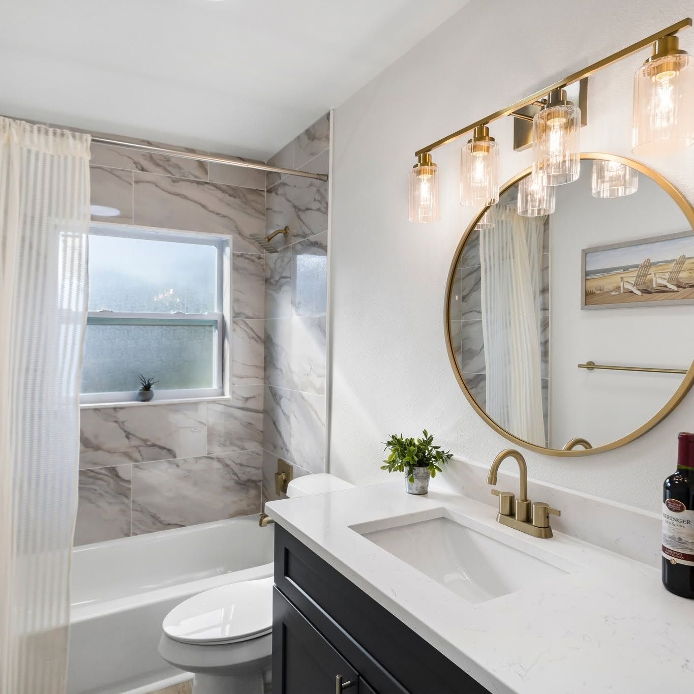 Modern bathroom with marble shower, round mirror, gold sconces, and white vanity