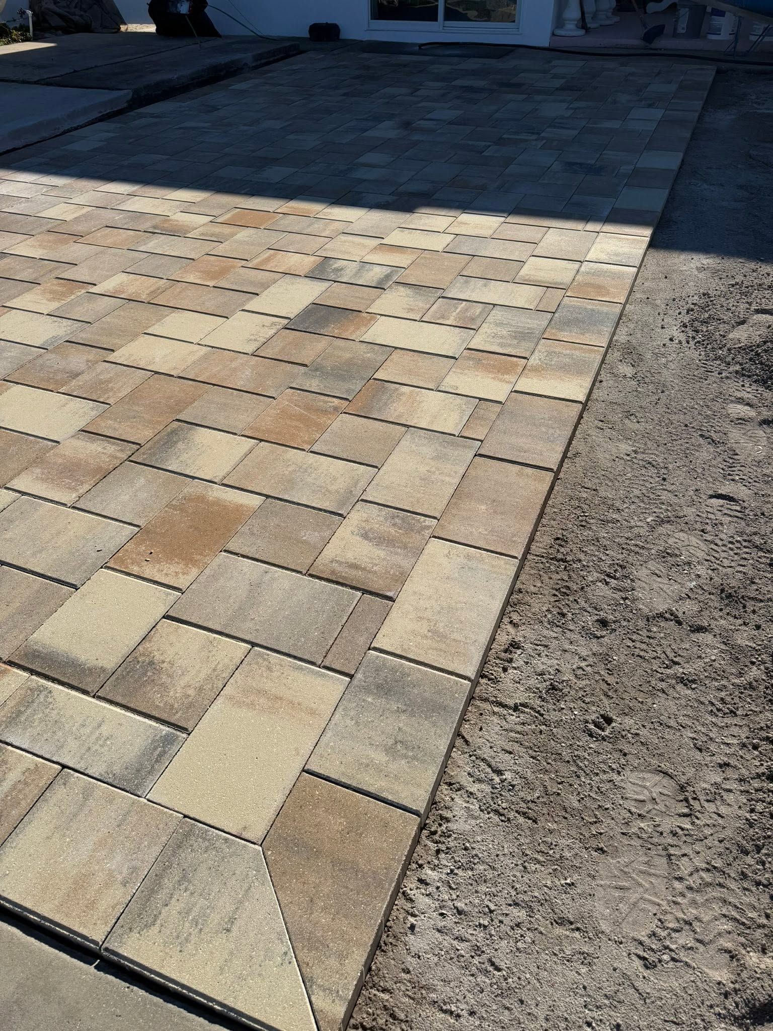 Brick-patterned paved driveway under construction, with a gravel edge along one side.