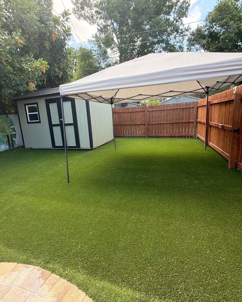 Backyard with artificial turf, a white canopy tent, wooden fence, and a small shed.