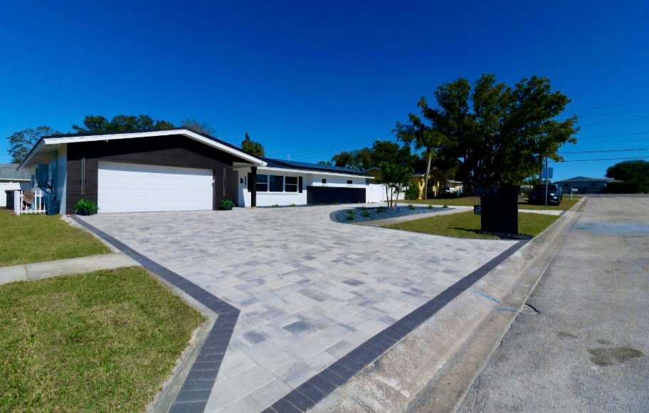 Modern house with a large paved driveway, garage, and tree-lined street under a blue sky