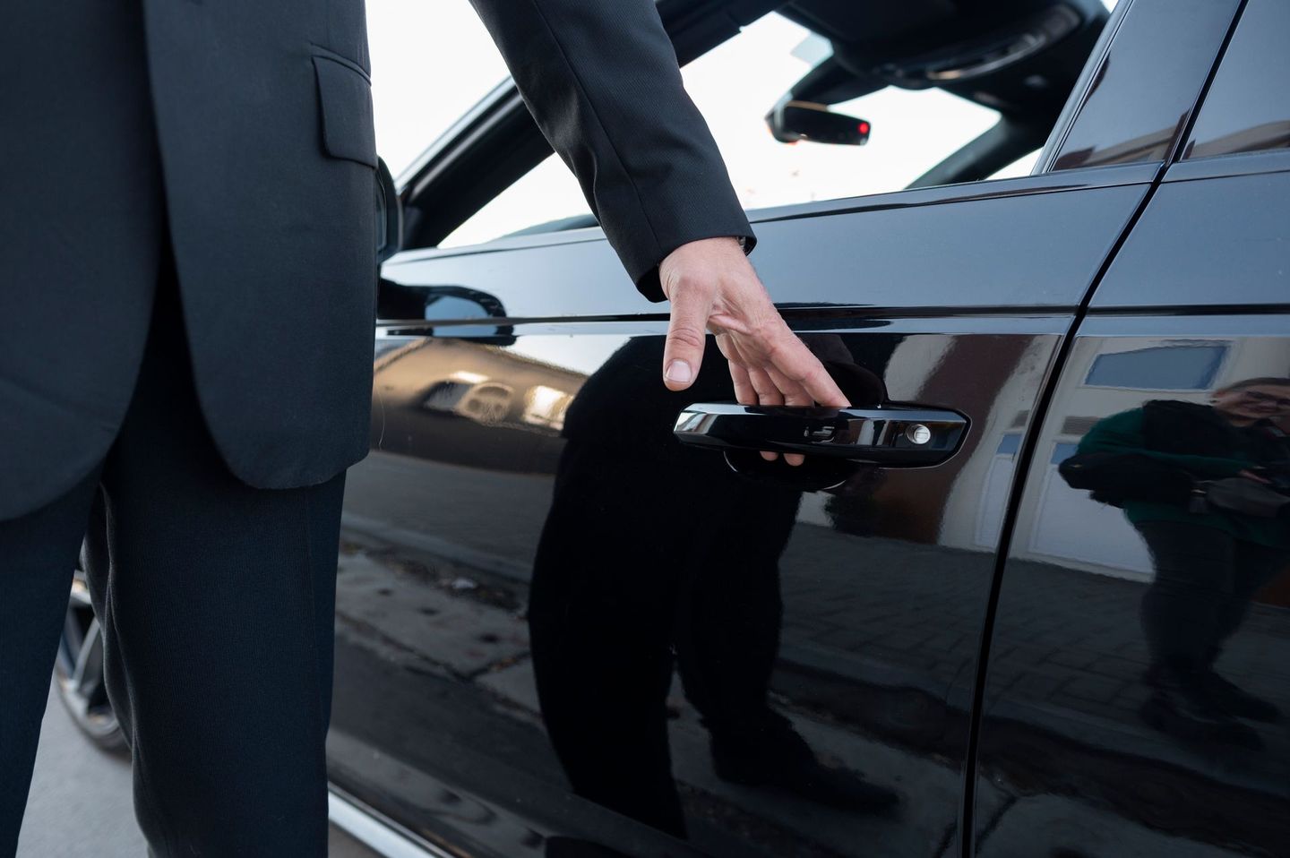 Person in a suit opening the door of a black car.