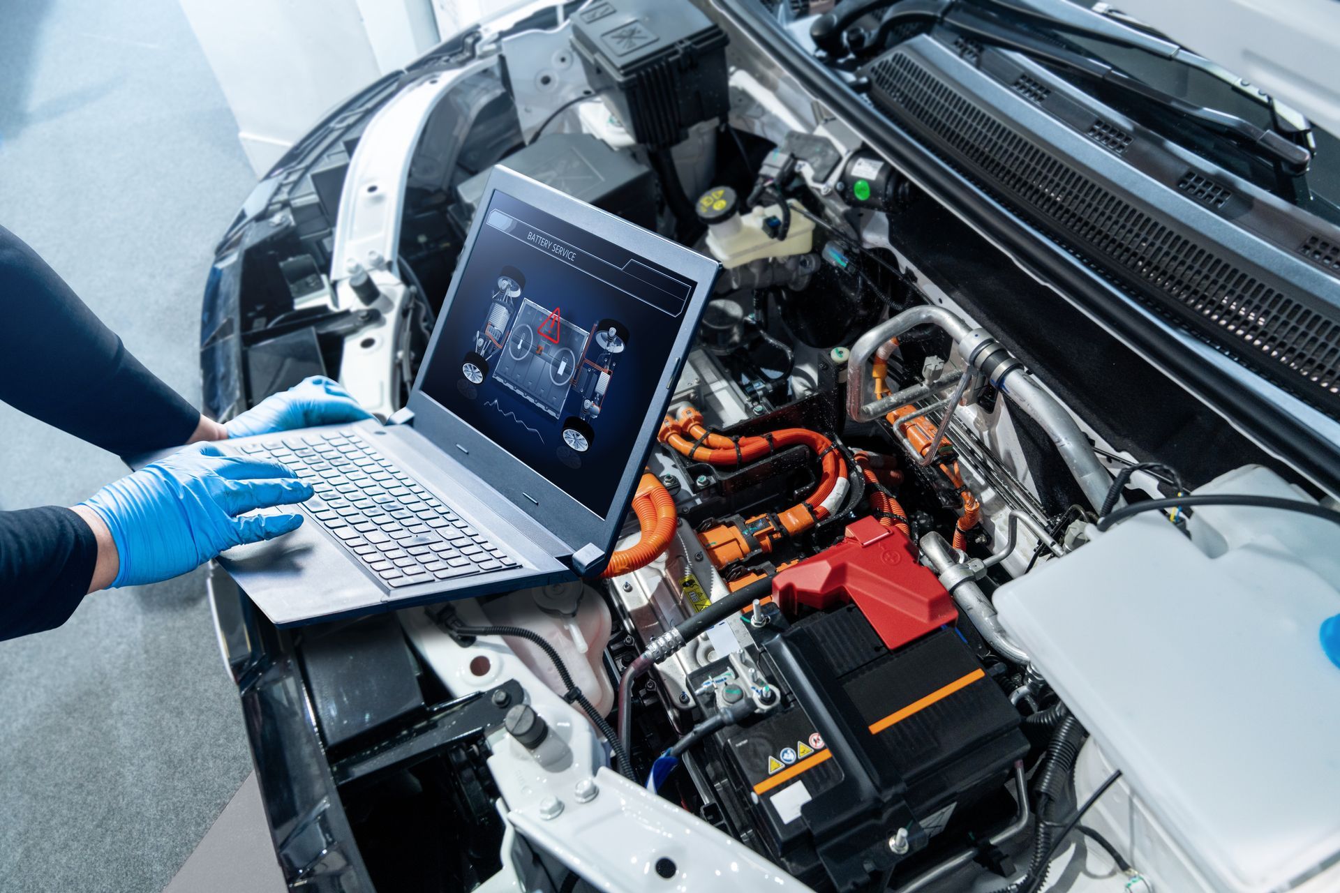 Technician using a laptop to diagnose a car engine with exposed wiring