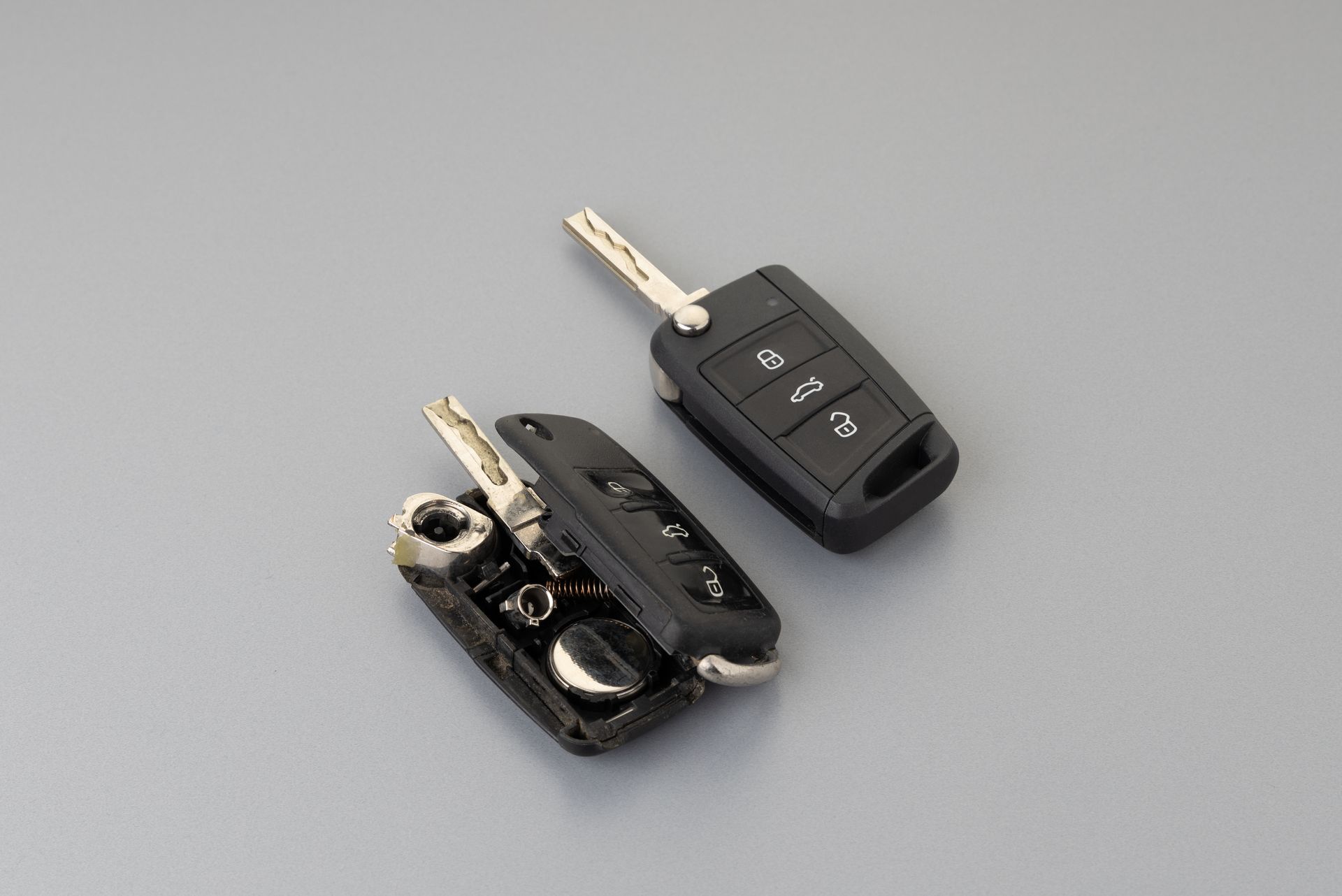 Two car keys, one folded and one remote key fob, on a gray background