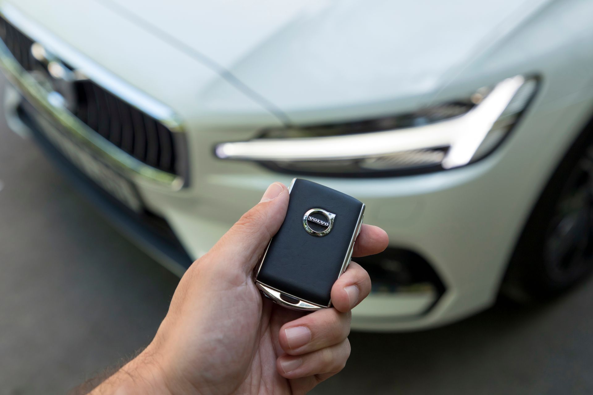 Hand holding a Mazda car key fob in front of a silver car grille and headlight