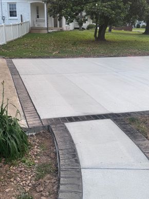 Concrete driveway and walkway leading to a white house with a porch and lawn.
