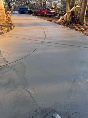 Cracked concrete driveway curving uphill past parked cars and leafless trees in warm evening light
