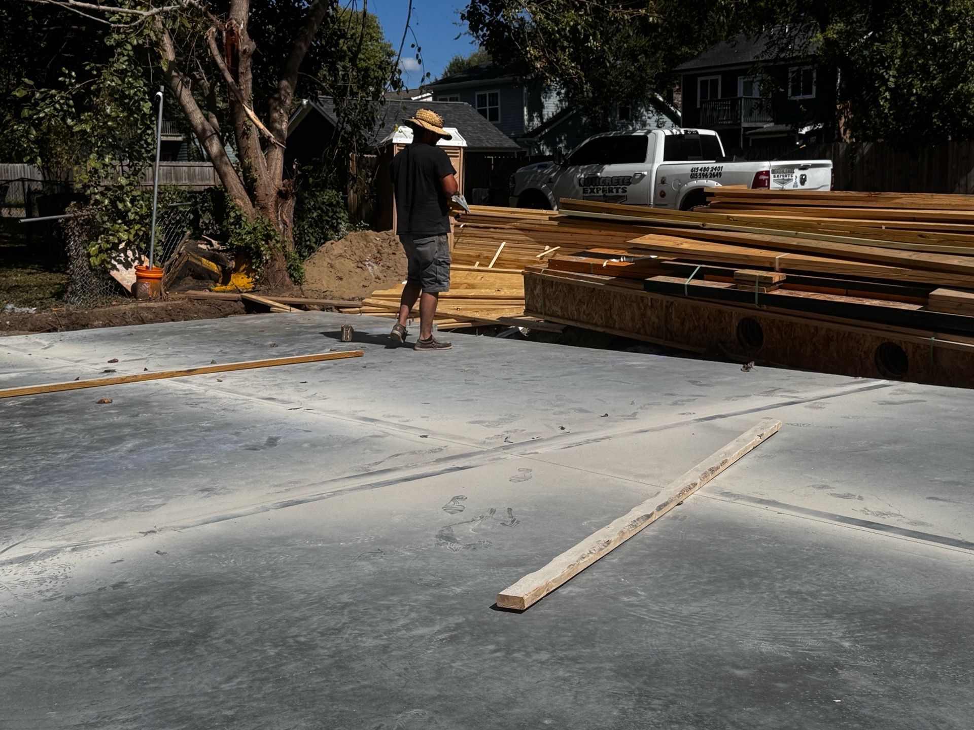 Worker standing by lumber stacks at a construction site with a concrete slab in the foreground