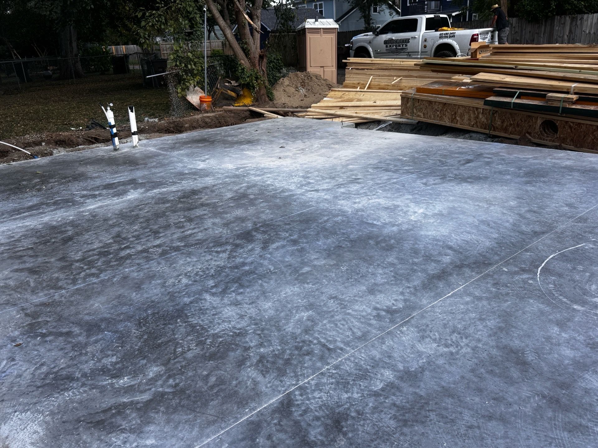 Freshly poured concrete slab with a house foundation, wooden forms, and construction materials nearby