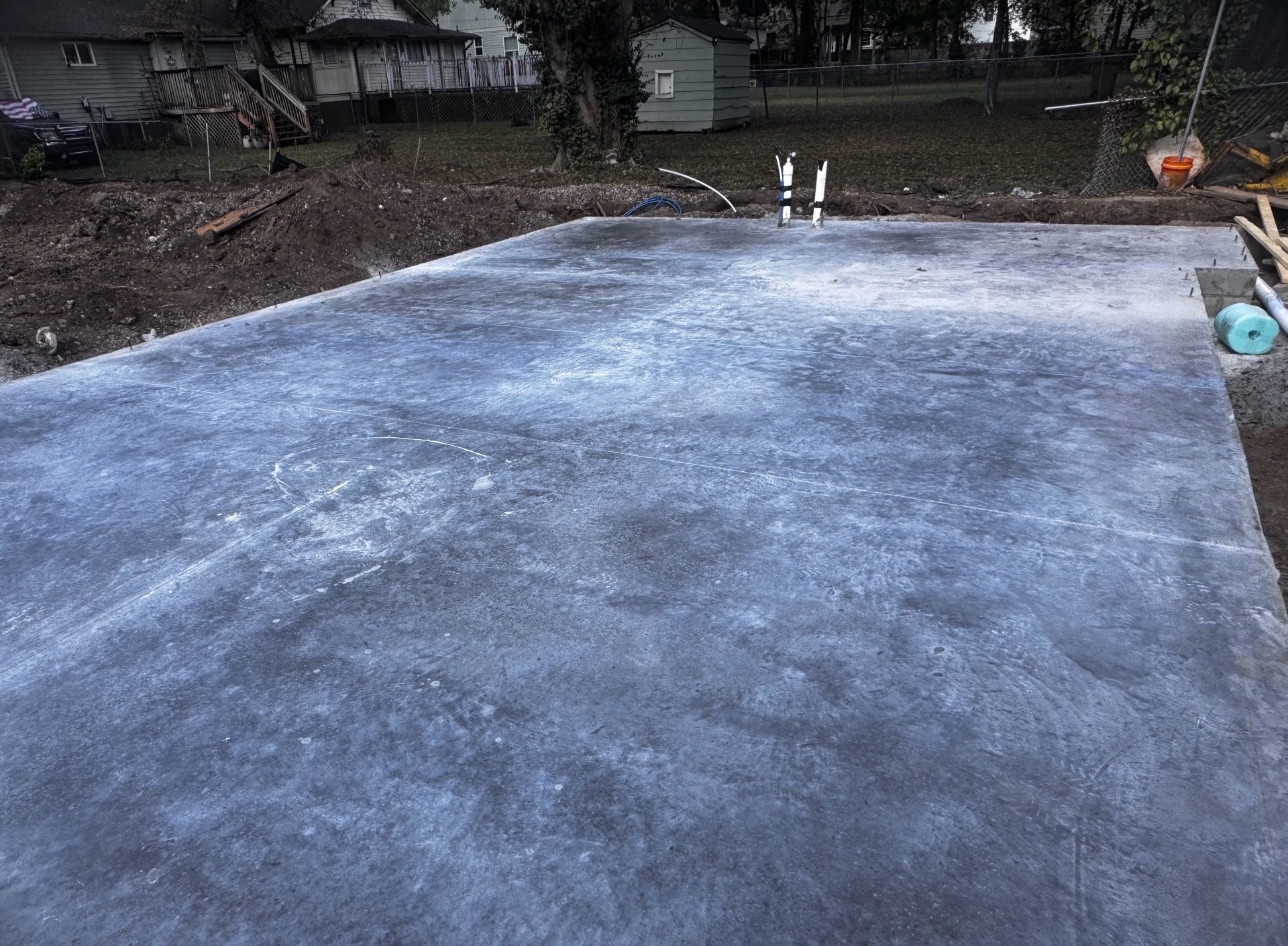 Freshly poured concrete slab in an outdoor yard, with exposed pipes near the back edge.