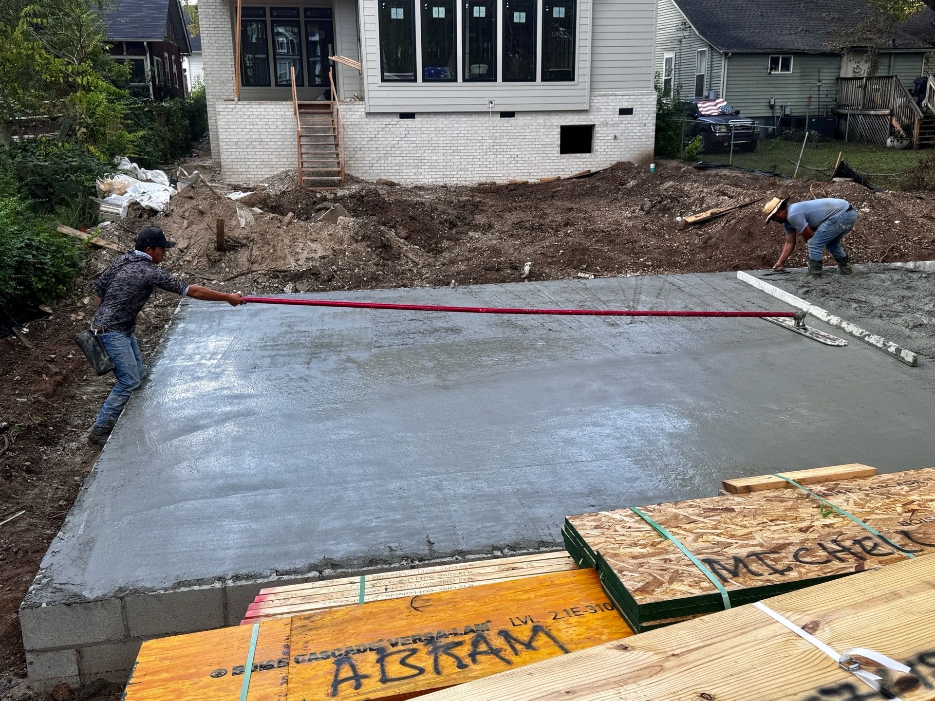 Freshly poured concrete driveway in front of a house, with two workers leveling the edges.