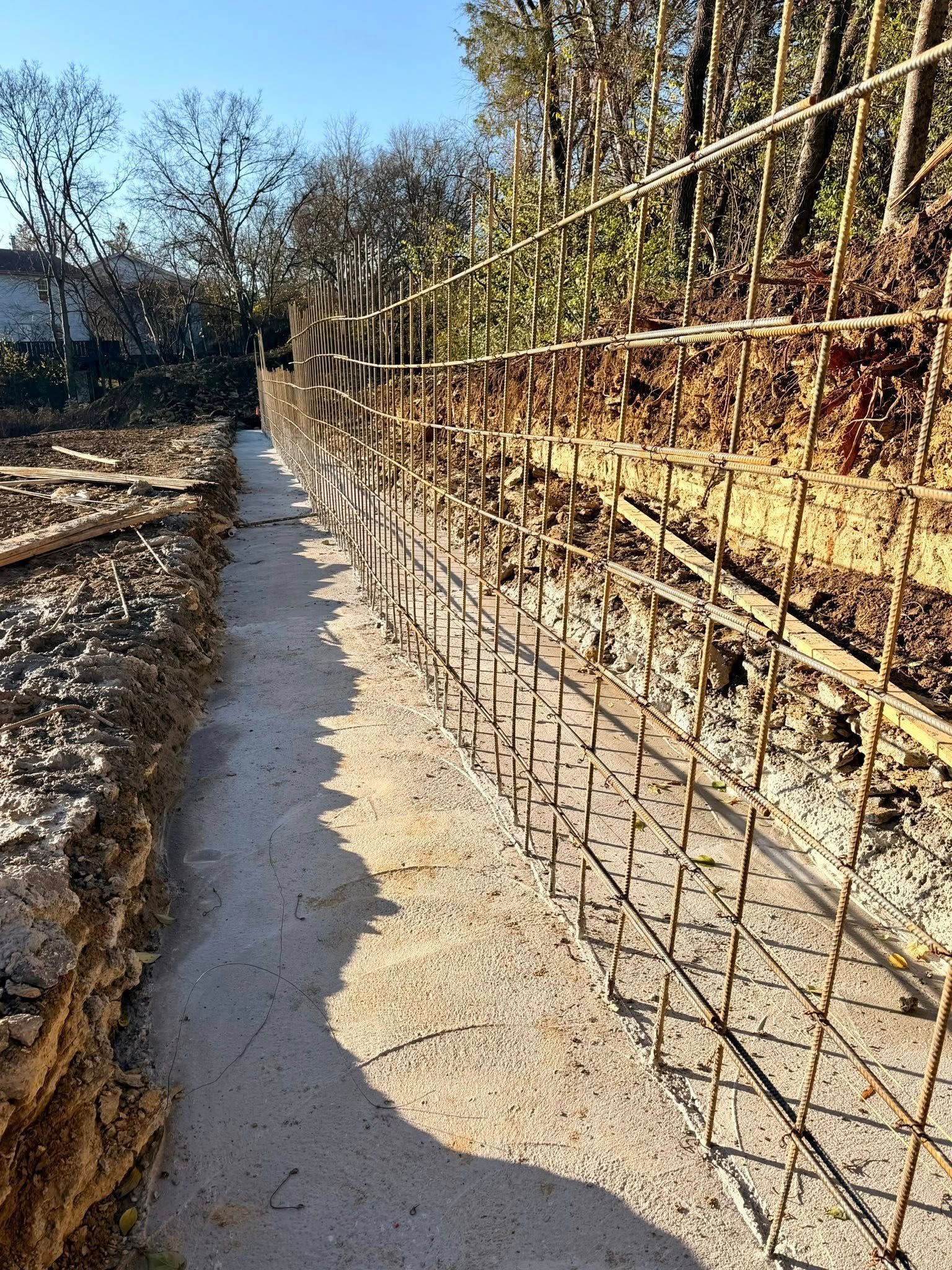 Gravel path beside a construction site, with steel rebar walls and trees in sunlight