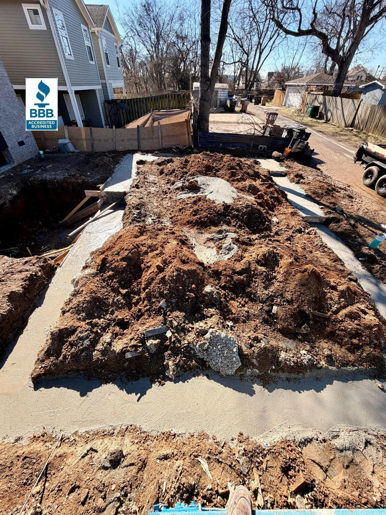 Freshly turned soil and mulch in a narrow backyard garden bed beside houses and leafless trees.