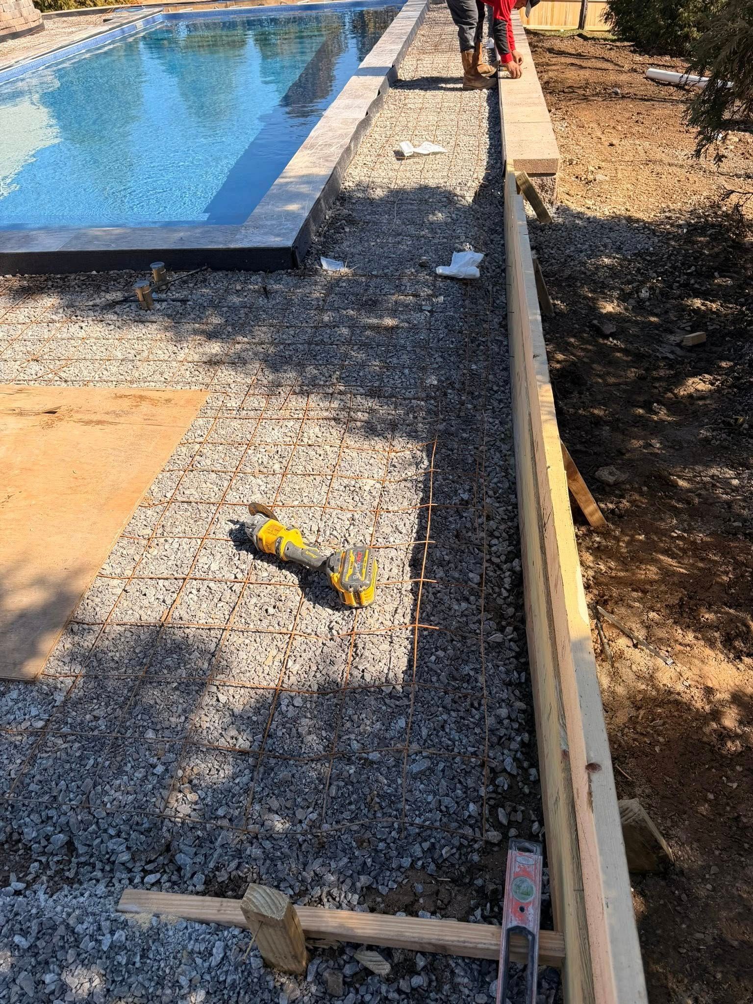 Poolside walkway under construction with gravel, wooden edging, and a worker near the pool