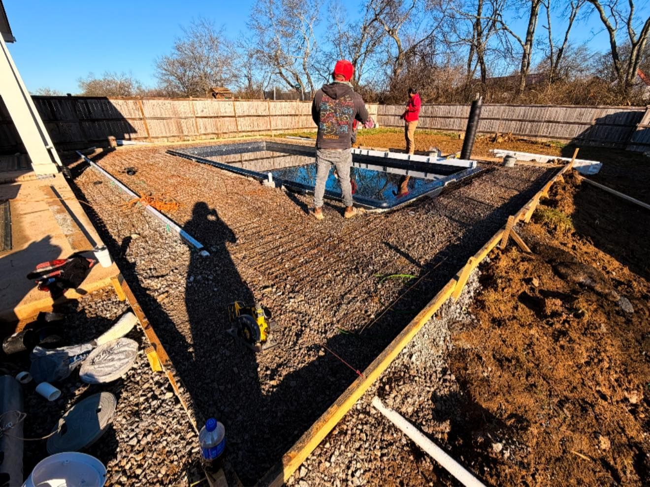 Workers pouring concrete for a backyard patio foundation with wooden forms and tools visible