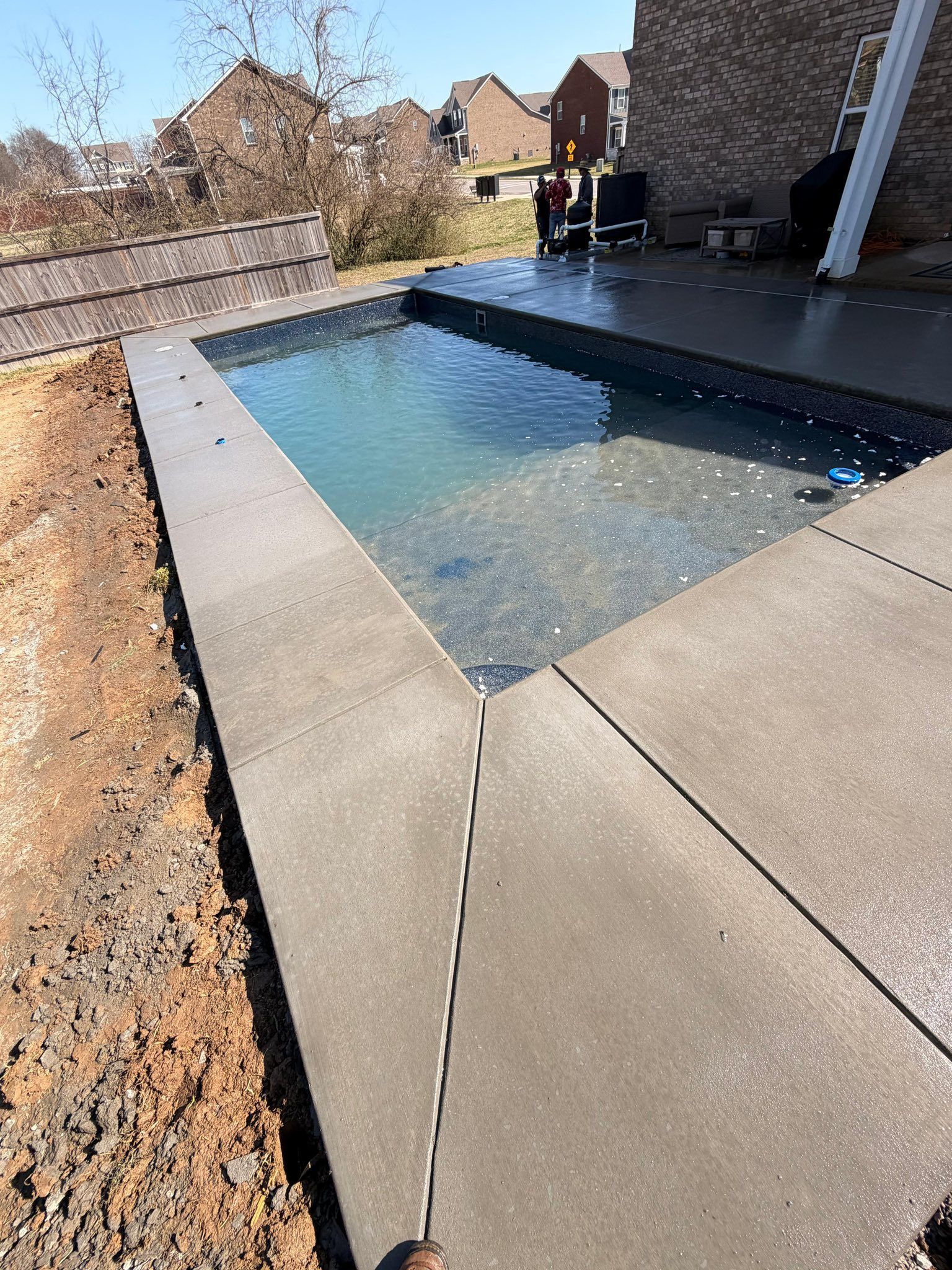 Rectangular backyard swimming pool with stone pavers and a patio in bright sunlight