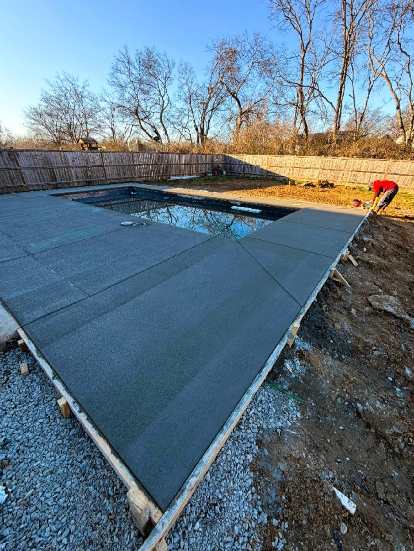 Covered swimming pool under construction in a backyard, with a worker in red at the edge.