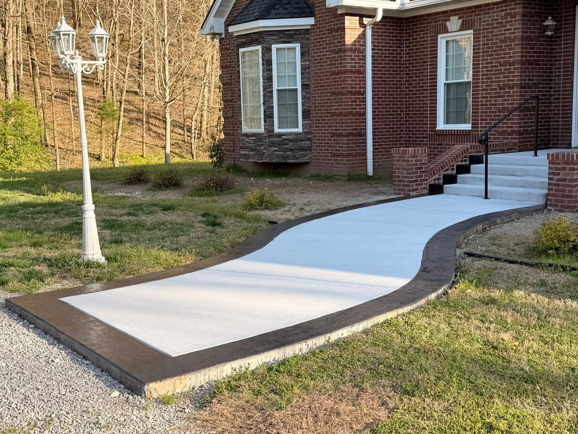 Concrete ramp leading to a brick house entrance with black handrails and a white lamp post nearby