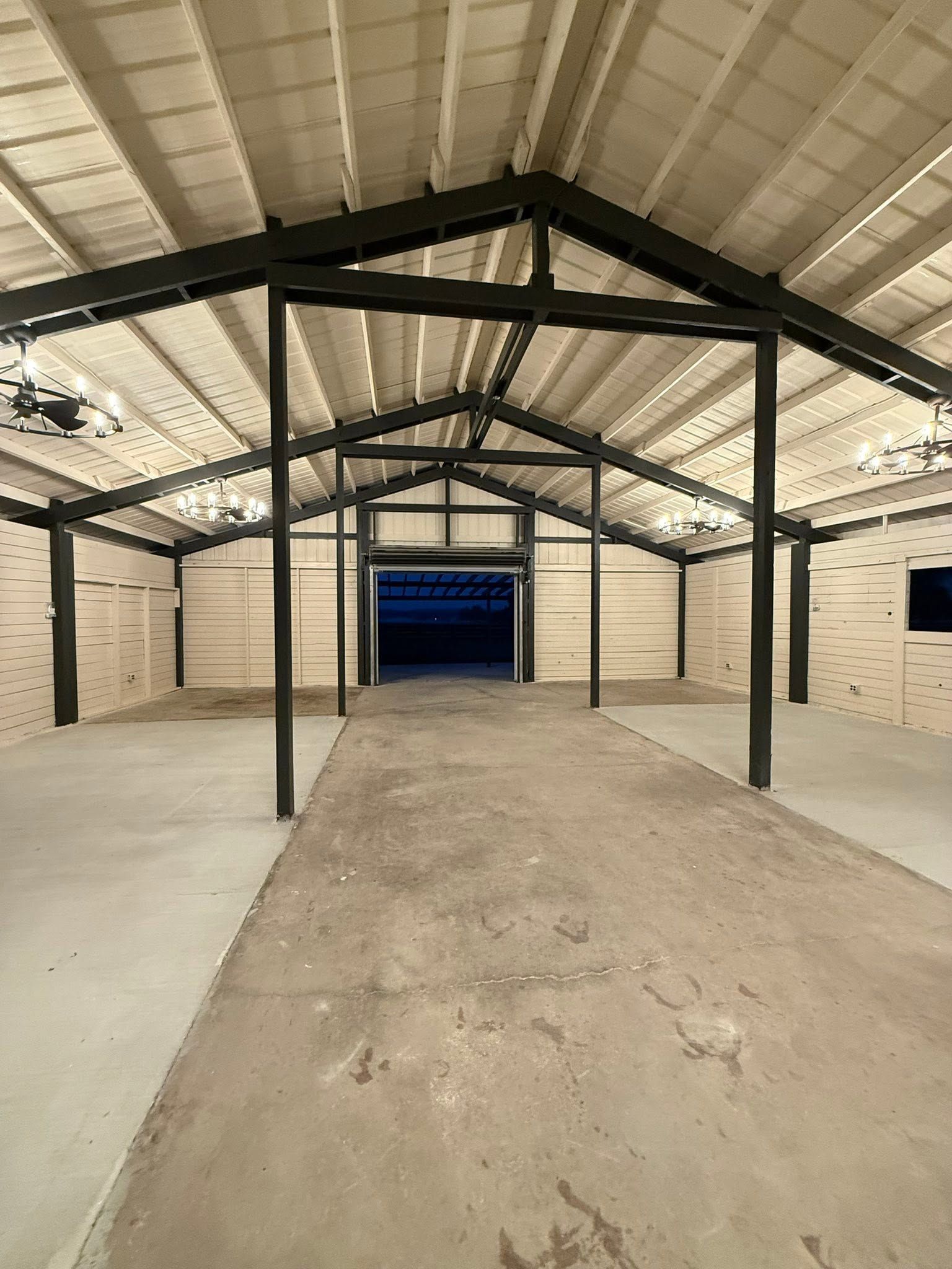 Empty warehouse interior with black steel framing, white walls, and a concrete floor leading to a blue door.