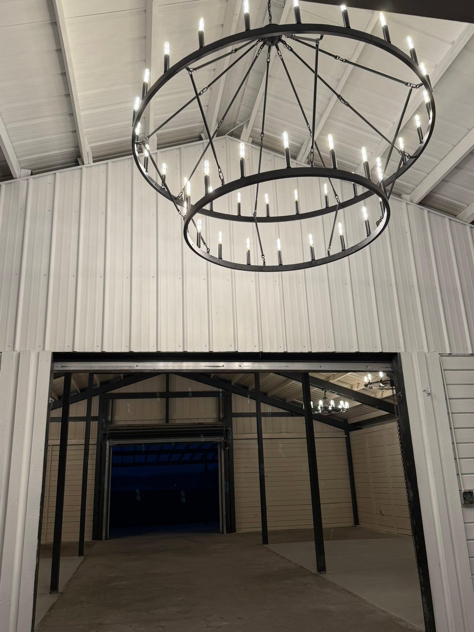 Warehouse interior with white paneled walls and a large circular hanging chandelier over an open doorway.