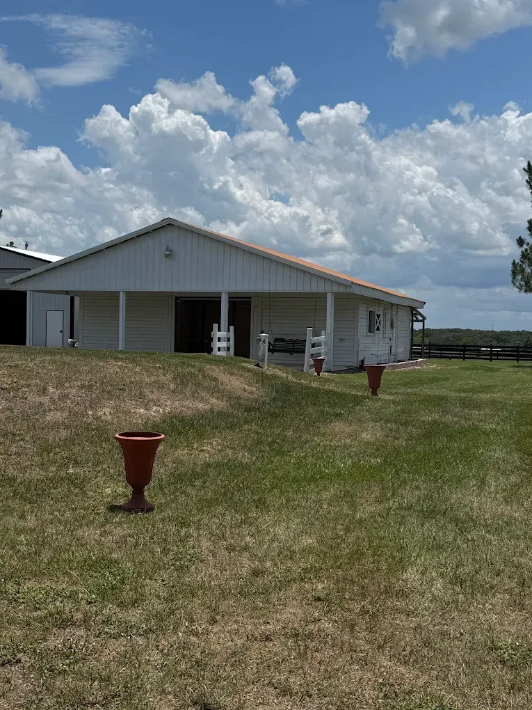 Rural white building with a covered porch on a grassy hill under a cloudy sky.